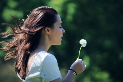 Side view of young woman holding dandelion