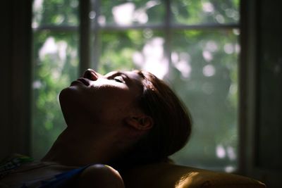 Young woman with closed eyes against window at home