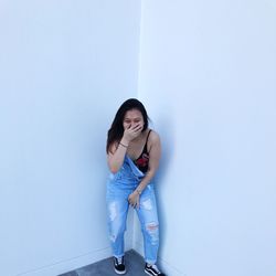 Portrait of young woman laughing while standing by white wall