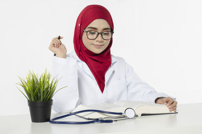 Portrait of young woman holding eyeglasses against white background