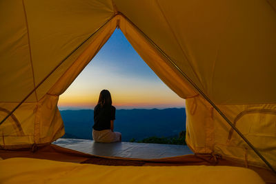 Rear view of woman sitting at tent against sky during sunset