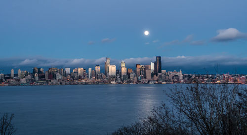 A full moon shines above the seattle skyline.