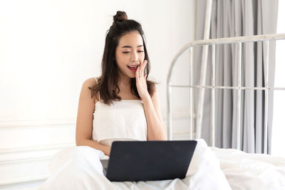 Young woman using phone while sitting on bed at home