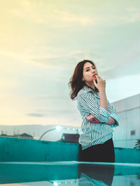 Young woman looking away while standing against sky