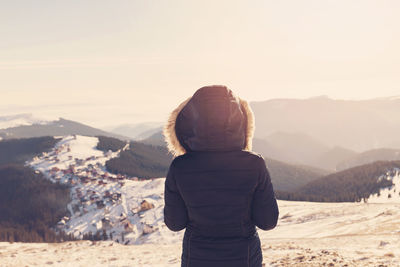 Rear view of woman standing on snow covered landscape against sky