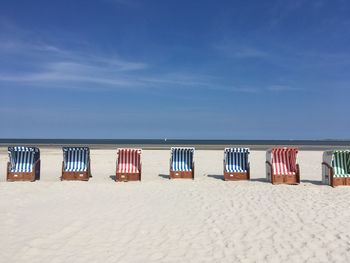 Hooded chairs on beach against blue sky