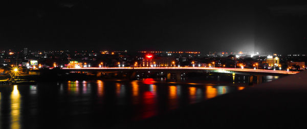 Illuminated city by river against sky at night