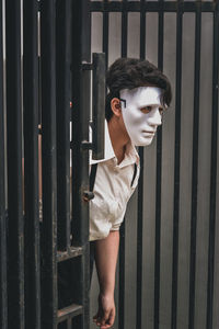 Portrait of a person wearing a mask walking out of a black gate