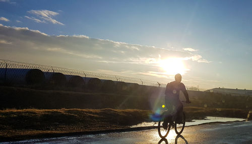 Rear view of man riding bicycle against sky during sunset