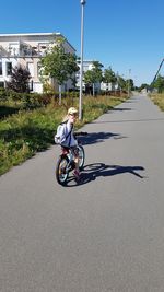 Girl riding bicycle on road against clear blue sky during sunny day