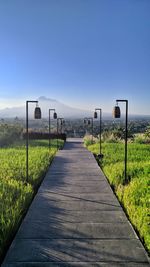 Empty footpath amidst grass against clear sky