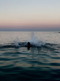 Silhouette swimming against sky during sunset