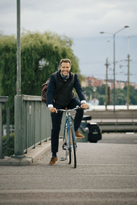 Portrait of smiling businessman riding bicycle on bridge in city