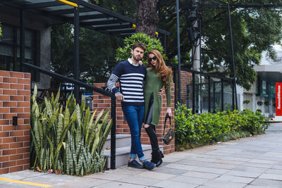 Full length portrait of young couple standing against building