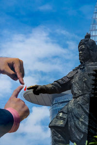 Low angle view of hand holding statue against sky