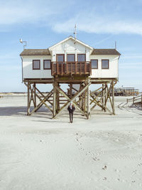 Woman sitting by lifeguard hut on beach by sea against sky