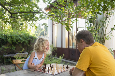 Granddaughter and grandfather playing chess in garden