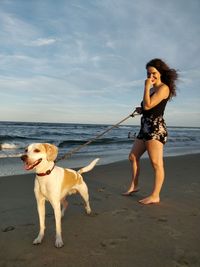 Young woman with dog standing at beach against sky