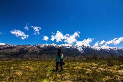 Rear view of woman standing on field against blue sky
