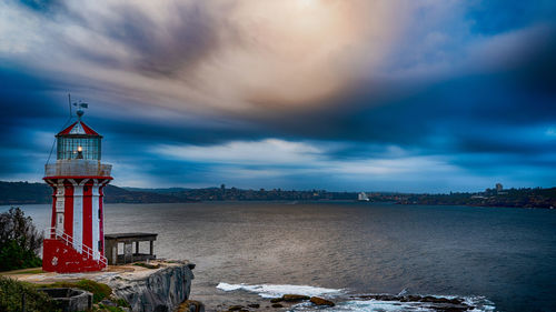 Lighthouse amidst sea and buildings against sky