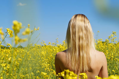 Rear view of topless young woman on field against clear sky