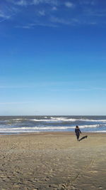 Woman walking on beach against blue sky