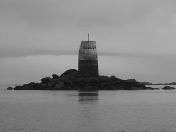 Tower on rocks amidst sea against cloudy sky