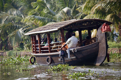 People sitting in boat on river by palm trees