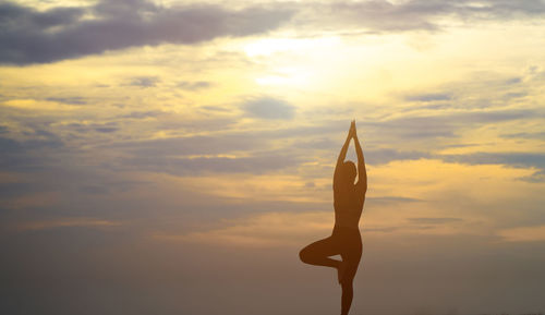 Low angle view of silhouette man with arms raised against sky during sunset