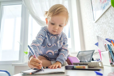 Girl writing in book while sitting on table at home