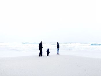 Full length of family standing on shore at beach during winter