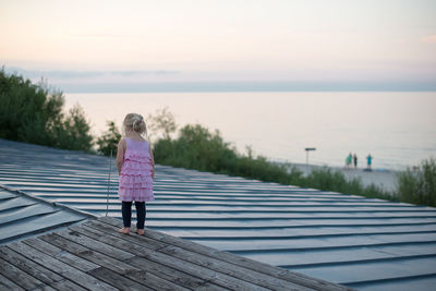 Rear view full length of girl standing on roof against sea