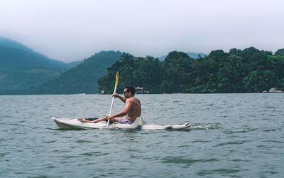 Man rowing boat in lake against sky