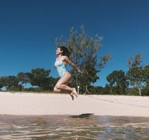 Full length of woman jumping at beach against sky