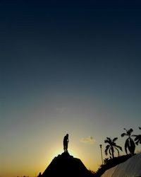 Low angle view of silhouette man on built structure against blue sky