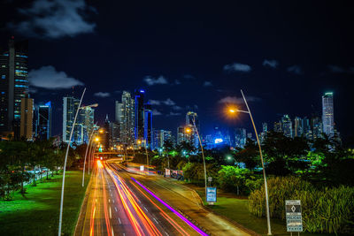 Light trails on road amidst illuminated buildings in city at night