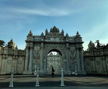 Person standing by gate historic building against sky