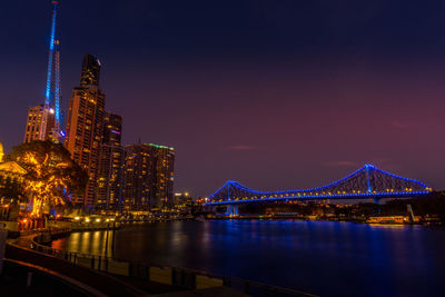 Illuminated city by river against sky at night