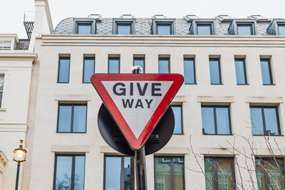 Red give way traffic sign mounted on pole with modern building in background