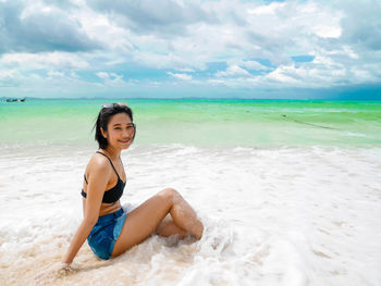 Portrait of smiling young woman sitting on beach against sky