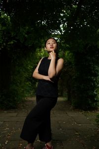 Young woman with hand on chin standing against trees at park