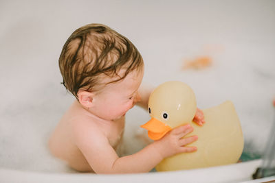 Baby in bath playing with big rubber duck