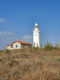 Lighthouse on field by building against sky