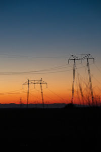 Low angle view of electricity pylon against sky during sunset