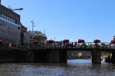 Bridge over river by buildings against clear blue sky