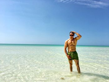 Full length of shirtless man standing on beach against clear sky