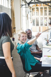 Cheerful businesswoman holding feather while sitting by male colleague at desk in creative office