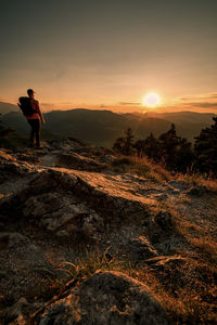 Man standing on rock against sky during sunset