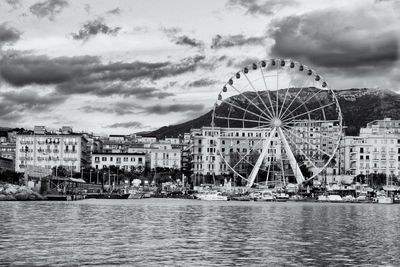 Ferris wheel by river in city against sky