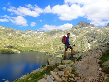 Hiker standing on rock formation by lake against sky